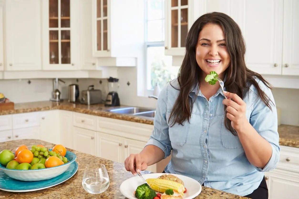 A woman sitting at the table eating broccoli.